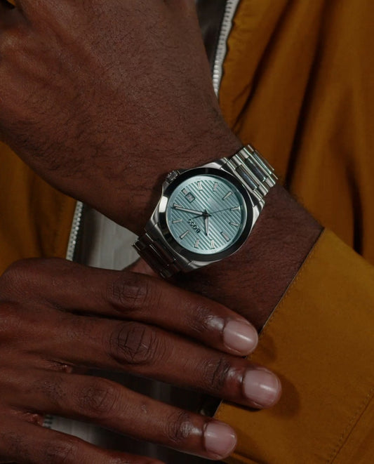 Reloj Hugo Boss en muñeca masculina, caja redonda, esfera azul, estilo moderno y elegante, diseño de tres agujas.